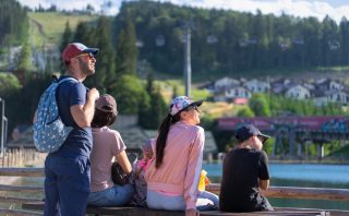 A family enjoys a sunny day sitting on a bench in Bukovel, Ukraine, with scenic mountain views.